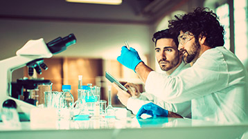 Zwei Chemiker arbeiten gemeinsam mit Proben an einem Mikroskop im Labor.