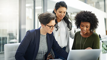 Drei junge Geschäftsfrauen unterschiedlicher Herkunft schauen gemeinsam auf einen Laptop.