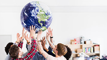 Eine Gruppe junger Leute hält einen großen Globus auf ihren Händen in die Höhe.