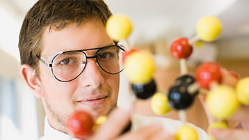 Mann mit Brille hinter Molekülmodell