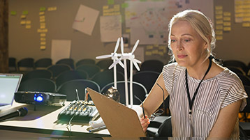 Eine Frau sitzt neben dem Modell einer Windkraftanlage und schaut in Unterlagen.
