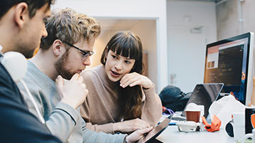 Drei junge Leute schauen gemeinsam auf ein Tablet.