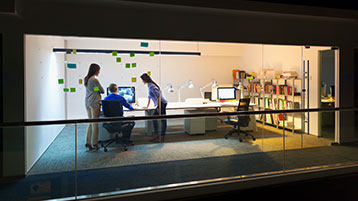 Blick in ein Büro mit Glasfront, in dem drei Menschen arbeiten.