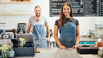 Ein Mann und eine Frau stehen in einem Café hinter der Theke mit Kasse.