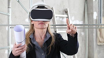 Eine Frau trägt eine VR-Brille und zeigt mit dem Finger in die Luft.