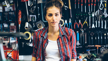 Eine junge Frau steht vor einer Werkzeugwand.