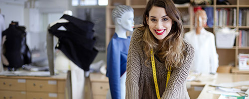 Frau steht in einem Modeatelier und hat ein Maßband um den Hals hängen. Frau steht in einem Modeatelier und hat ein Maßband um den Hals hängen.