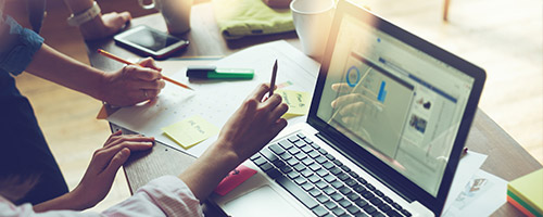 Arbeitende Hände zweier Personen an einem Schreibtisch mit Tassen, Stiften, Zetteln und einem Laptop. Arbeitende Hände zweier Personen an einem Schreibtisch mit Tassen, Stiften, Zetteln und einem Laptop.