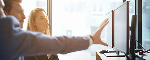 Ein Mann zeigt einer Frau und einem Mann etwas an zwei großen Computerbildschirmen. Ein Mann zeigt einer Frau und einem Mann etwas an zwei großen Computerbildschirmen.