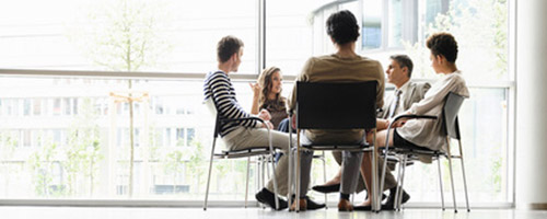 In einem großen Raum mit bodentiefer Fensterfront sitzen Geschäftsleute im Gespräch an einem Tisch. In einem großen Raum mit bodentiefer Fensterfront sitzen Geschäftsleute im Gespräch an einem Tisch.