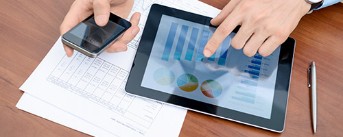 Männerhände arbeiten an einem Smartphone und einem Tablet auf einem Tisch mit Zetteln und einem Stift. Männerhände arbeiten an einem Smartphone und einem Tablet auf einem Tisch mit Zetteln und einem Stift.