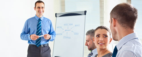 Seminarsituation: Ein Referent in Anzug und Krawatte steht vor einer Gruppe von Geschäftsleuten vor einem Flipchart, auf dem ein Schaubild aufgezeichnet ist. Seminarsituation: Ein Referent in Anzug und Krawatte steht vor einer Gruppe von Geschäftsleuten vor einem Flipchart, auf dem ein Schaubild aufgezeichnet ist.